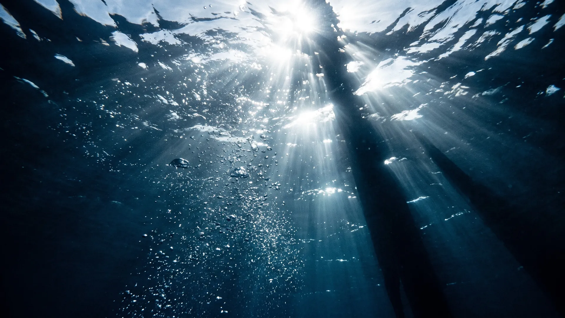 Sunlight streaming through deep blue water, seen from below the surface